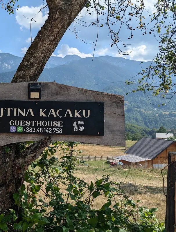The carved Bujtina Kaçaku guesthouse sign hanging from a tree, mountains behind
