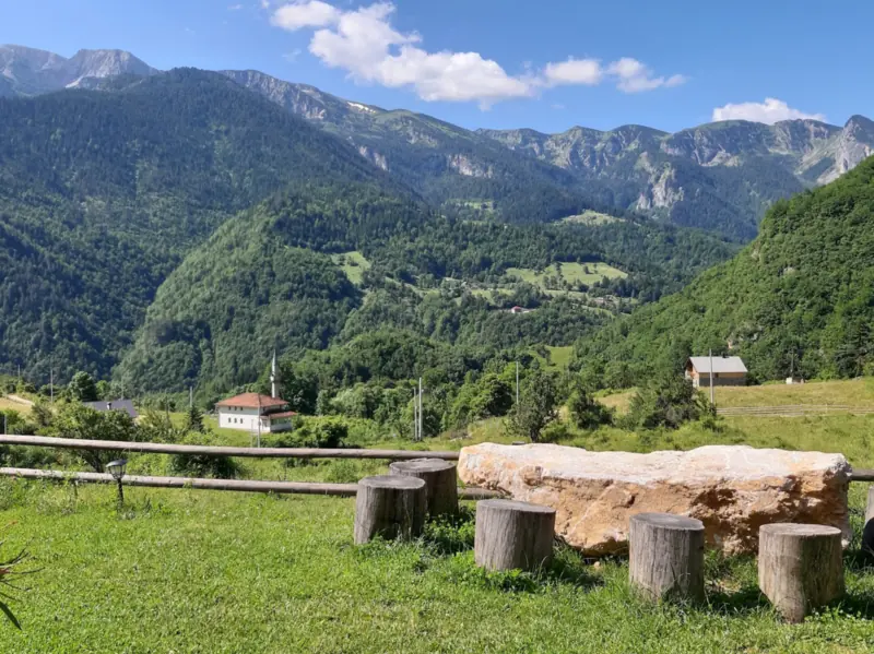 The Rugova peaks and valley seen from the guesthouse garden, with log stools and a stone table