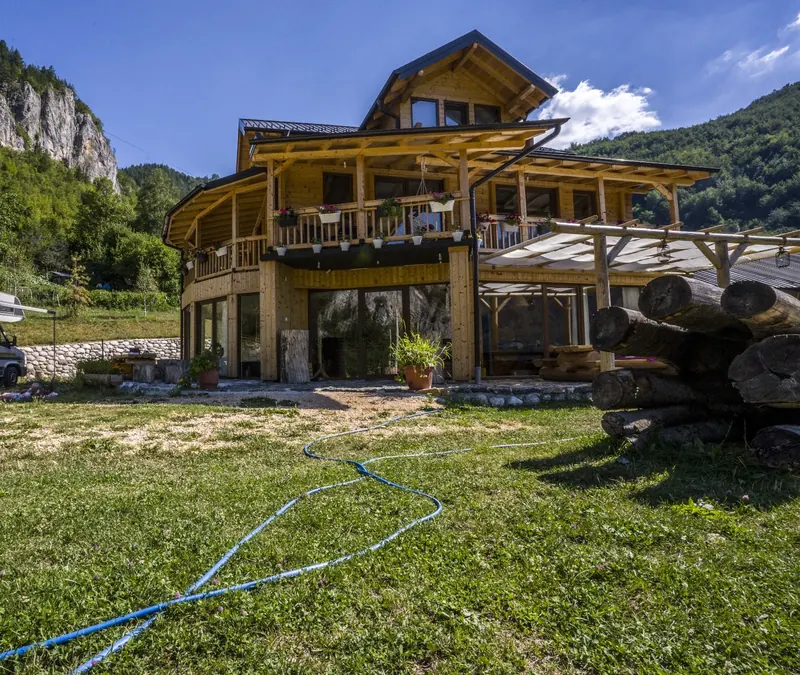 The wooden guesthouse under limestone cliffs, with a camper parked on the meadow