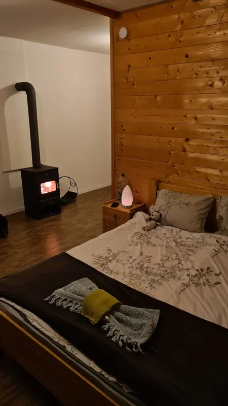 Room with pine-clad wall, double bed and a wood stove